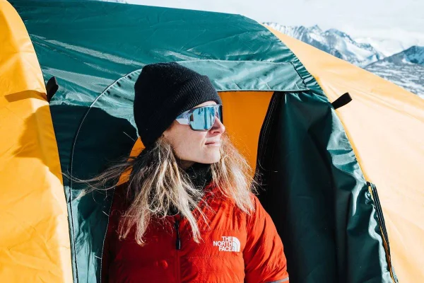 Imagem colorida: mulher em frente à barraca de acampamento em montanha - Metrópoles