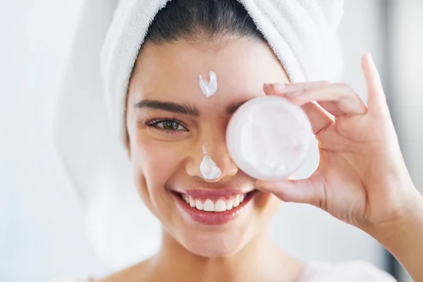 Mulher sorridente segura frasco de creme próximo ao olho