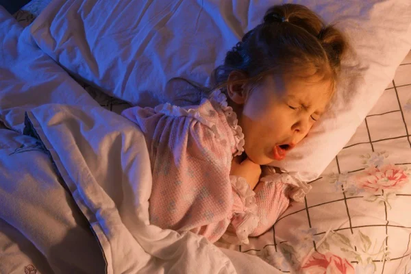 Imagem colorida mostra criança na cama tossindo - Metrópoles