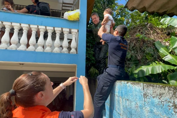 Imagem colorida de agentes da Defesa Civil resgatando criança. Metrópoles
