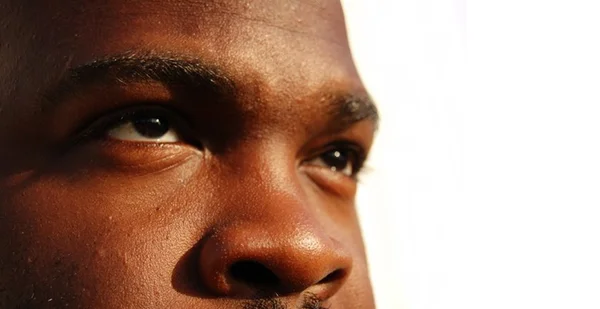 Imagem colorida mostra rosto de homem negro, de metade da testa até pouco acima dos lábios