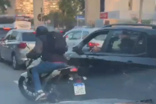 Imagem colorida do assaltante de moto ao lado do carro parado no trânsito enquanto o motorista aponta a arma pela janela. Metrópoles