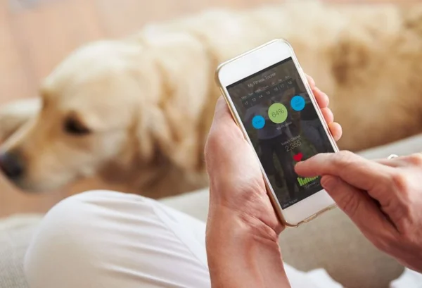 aplicativo para quem tem pets, mulher segurando um telenone e o cachorro ao fundo da imagem - metrópoles