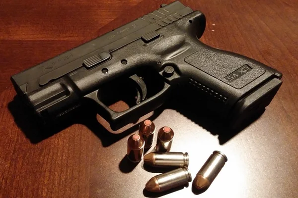 Foto colorida de uma arma preta ao lado de balas - Metrópoles
