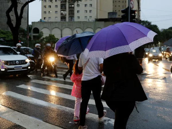 foto colorida de pedestres atravessando rua em São Paulo com guarda-chuvas - Metrópoles