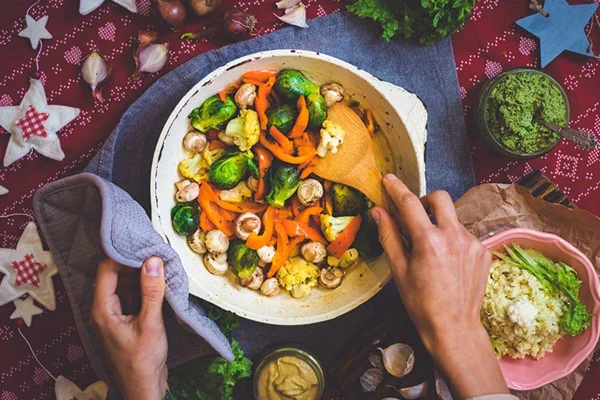 Na imagem, uma panela cinza com vegetais verdes, laranja e branco junto com um caldo. No fundo da mesa, uma toalha vermelha com estrelas desenhadas - Metrópoles