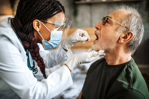 Médica adulta de meia idade em visita domiciliar fazendo teste de cotonete nasal em paciente idoso. Teste de saliva de Alzheimer