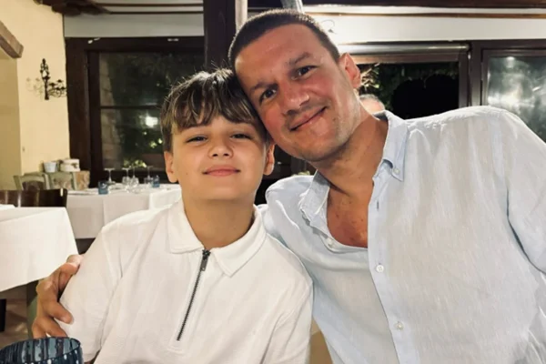 Foto colorida de homem ao lado de uma criança. Ambas sorrindo e fazendo pose para foto - Metrópoles.
