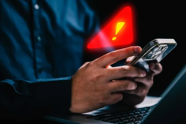 Imagem colorida de pessoa segurando celular com alerta de atenção em cima