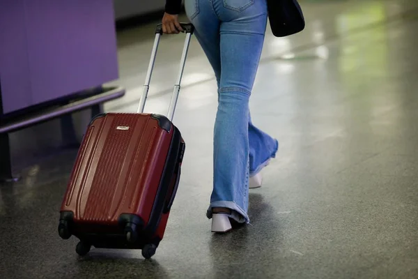 Na imagem colorida, há uma mala centralizada na cor preta. Pernas de pessoas se movimentando também foram registradas
