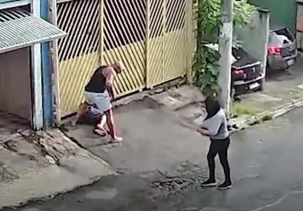 Imagem de homem rendendo outro na calçada; mulher olha para camiseta suja de sangue - Metrópoles