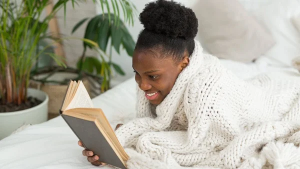 Mulher deitada no sofá lendo um livro