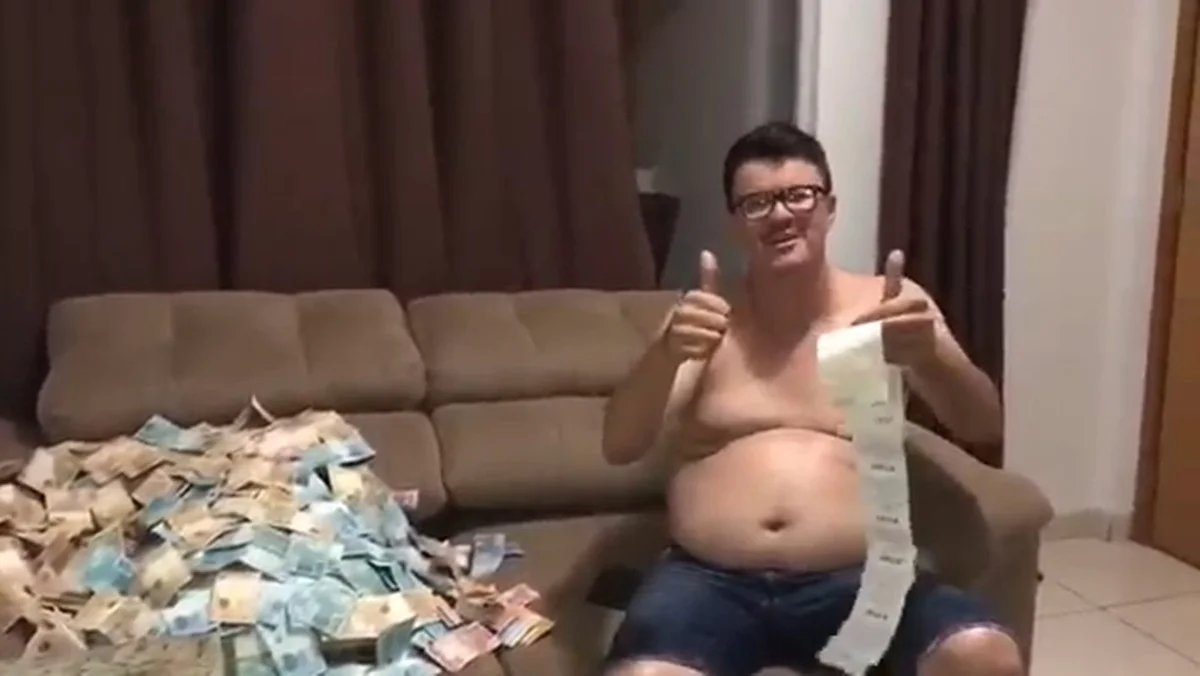 Homem sem camisa sentado ao lado ao lado de montanha de dinheiro