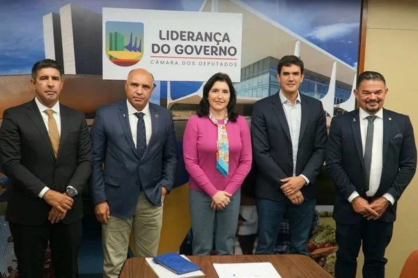 Fotografia colorida de mulher de rosa em pé ao centro da imagem com dois homens de cada lado