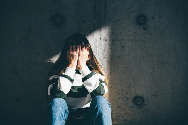 Jovem sentada no chão, com as mãos no rosto - Como apoiar alguém com depressão
