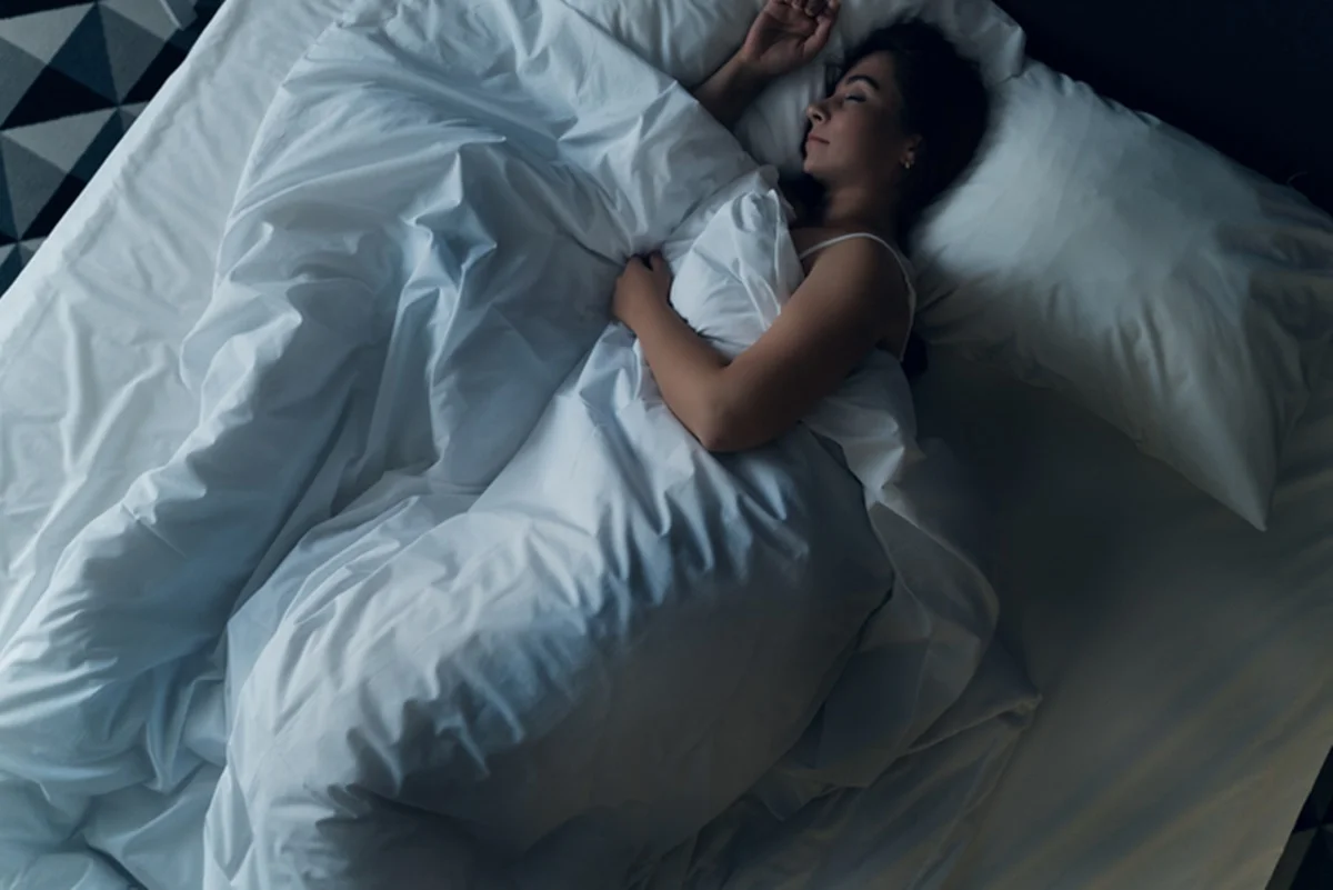 Foto colorida de mulher dormindo em cama com cobertor - Metrópoles