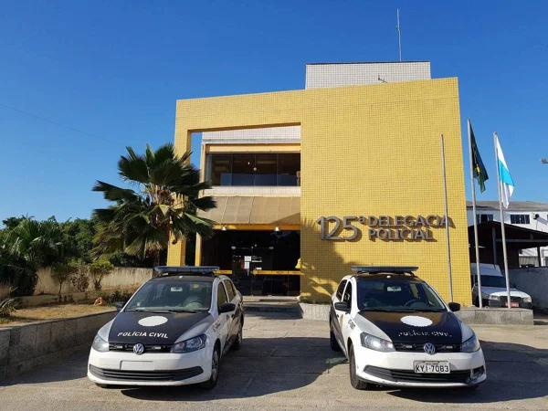 foto colorida de um prédio com a fachada amarela e duas viaturas de polícia na frente