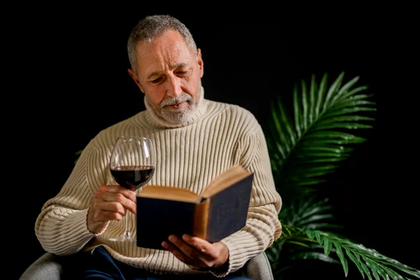 Homem lendo livro e segurando taça de vinho