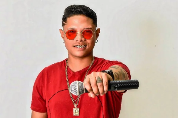 foto colorida de homem de pele negra clara de camiseta e oculos de lentes vermelhas - metrópoles
