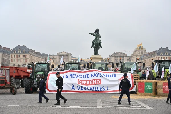 Agricultores atrás de uma faixa com os dizeres “A revolta camponesa recomeça em Versailles” protestam em frente ao Castelo, na França