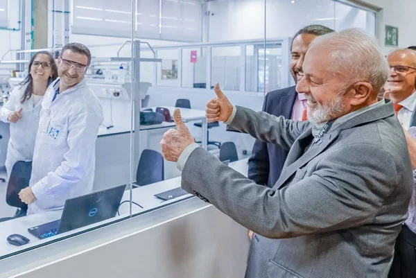 Homem branco de cabelos brancos faz joinha com as mãos em frente a vidro; do outro lado, estão cientistas - Metrópoles