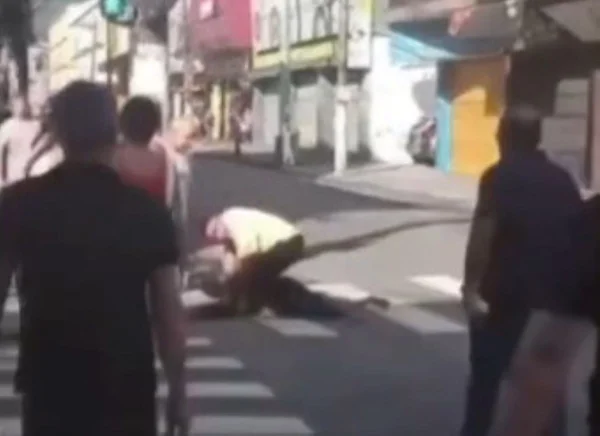 Homem com camisa branca imobilizando outro homem, no meio de avenida - Metrópoles