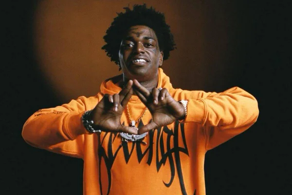 foto colorida de homem negro de blusa de moletom laranja fazendo triangulo com as mãos - metrópoles