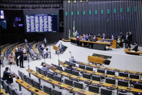 Parlamentares reunidos no plenário da Câmara dos Deputados no Congresso Nacional. As pessoas aglomeradas usam terno e gravata e estão em um local com cadeiras e microfones pretos- Metrópoles