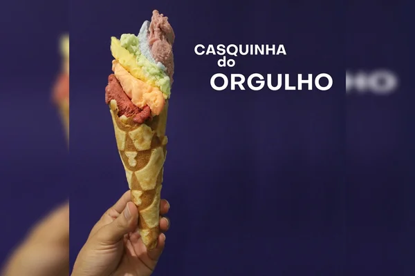 Mão branca segurando casquinha com sorvetes coloridos em frente a fundo roxo. Há um texto em letras brancas ao lado da casquinha de sorvete