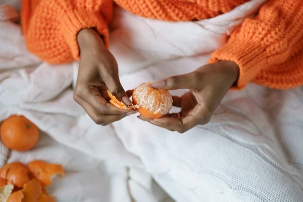 Foto de mulher com casaco laranja descascando tangerina - Metrópoles