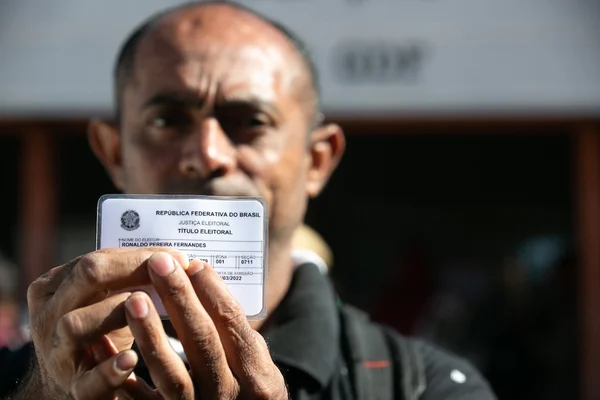 Homem negro careca mostrando cartão plastificado em frente ao rosto