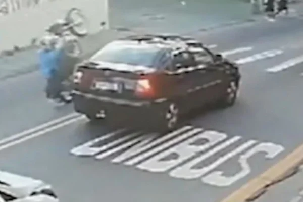 Imagem colorida mostra homem em moto fazendo uma manobra chamada "grau" ao lado de um carro - Metrópoles