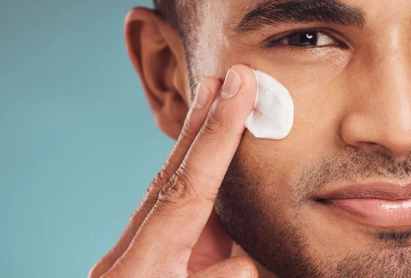 Foto colorida de homem passando creme no rosto em ritual de skincare - Metrópoles