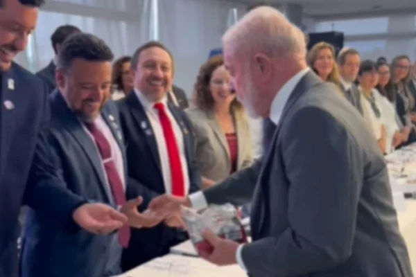 Foto colorida do presidente Luiz Inácio Lula da Silva entregando "baninhas" para se desculpar de atraso - Metrópoles