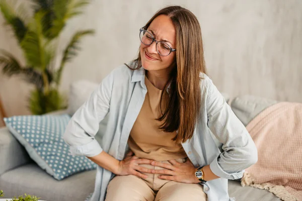 Foto colorida de mulher sentada em sofá com a mão no abdômen - Metrópoles - intestino preso
