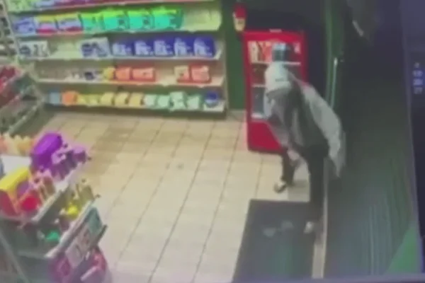 Imagem colorida de um homem encapuzado tentando sair de uma farmácia após ser trancado pelo dono do estabelecimento durante uma tentativa de assalto - Metrópoles
