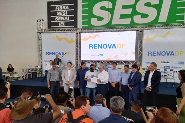 Ibaneis entrega diploma para alunos do Renova-DF. Na foto, o governador Ibaneis com alunos embaixo de uma placa do Sesi