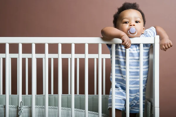 Foto colorida de bebê dentro do berço usando chupeta - Prós e contras da chupeta: entenda como o hábito afeta o bebê - Metrópoles