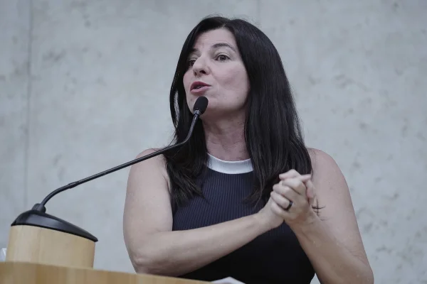 Imagem colorida mostra Silvia Ferraro, autora do requerimento da CPI do superfaturamento, mulher branca, de cabelos lisos e pretos, na altura do ombro, em uma imagem da cintura para cima, em um púlpito do plenário da Câmara Municipal, falando ao microfone. Ela veste uma blusa preta e lisa, de gola branca, e tem os braços à mostra. Ela segura uma mão com a outra na imagem - Metrópoles