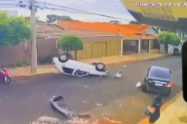 Imagem colorida de uma câmera de segurança mostra um carro branco capotado e outro carro preto atingido na traseira - Metrópoles