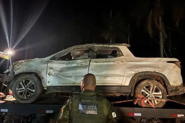 imagem colorida mostra carro guinchado e policial olhando