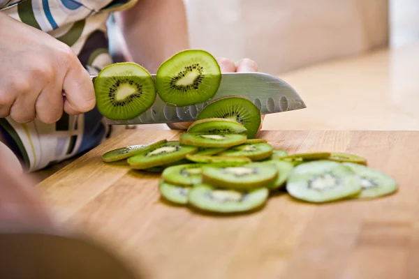 Foto colorida de mão feminina cortando kiwi - Metrópoles