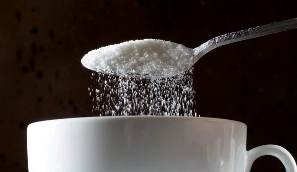 Foto mostra colher derramando açúcar em caneca - Metrópoles