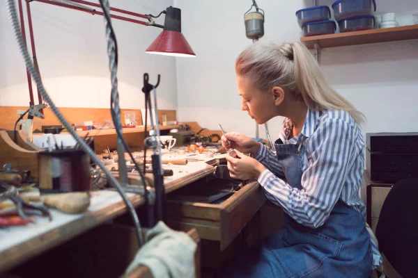 Na imagem com cor. mulher branca trabalha manualmente na construção de joias - Metrópoles