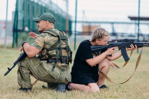 Foto colorida de jovem ucraniana segurando arma em campo de militarização russo - Metrópoles