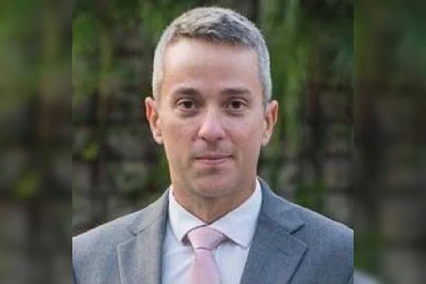 Vinícius Cardoso de Pinho Fragoso. Homem branco e grisalho de terno cinza e gravata rosa