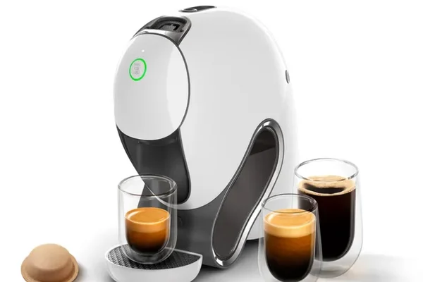 Cafeteira sustentável da Nestlé com Wi-Fi. Ela é branca, arredondada e cercada de copos de café e uma cápsula de papel - metrópoles