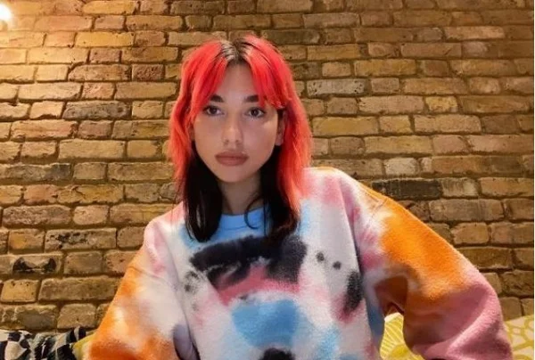 A cantora Dua Lipa. Ela tem cabelos coloridos e usa camiseta colorida - Metrópoles
