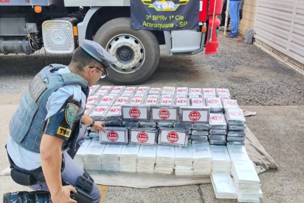 Imagem colorida mostra policial com carga de cocaína apreendida em fundo falso de caminhão - Metrópoles