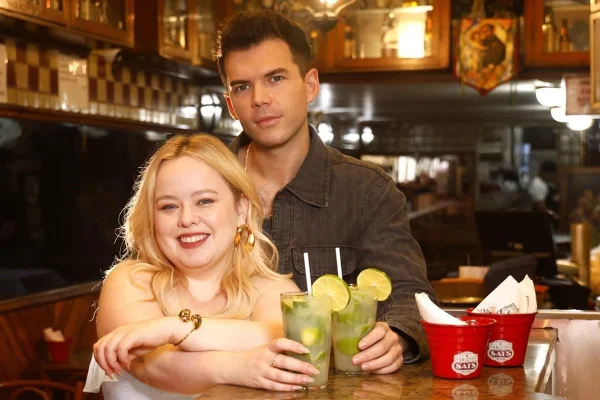 Foto colorida de mulher e homem segurando copo de caipirinha. Eles estão em um bar - Metrópoles